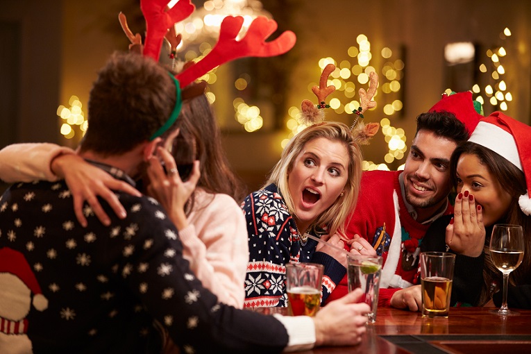 Couple Kissing In Bar As Friends Enjoy Christmas Drinks