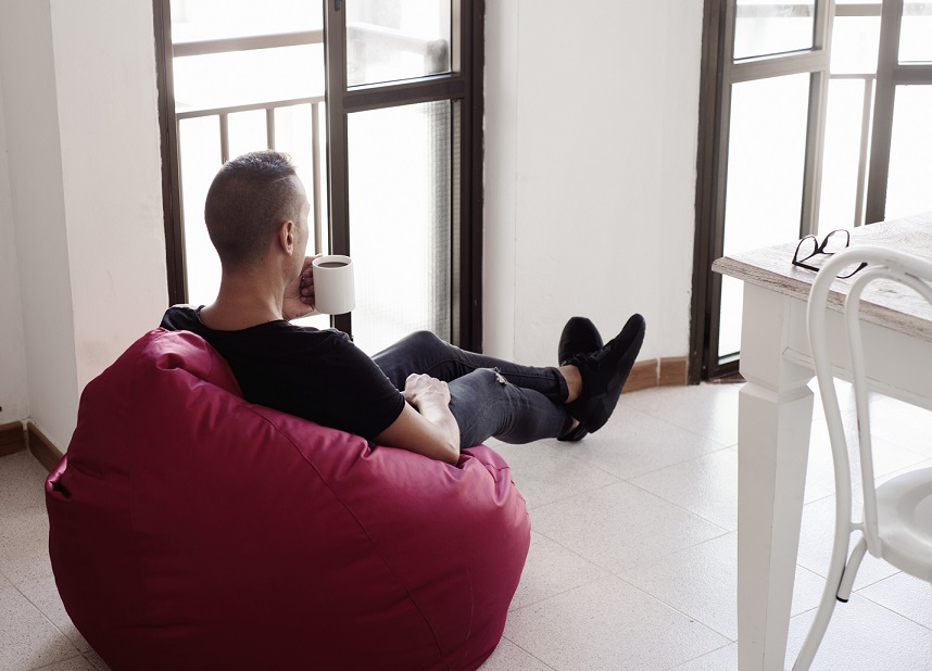a young man indoors have a coffee sitting in a comfortable red bean bag chair