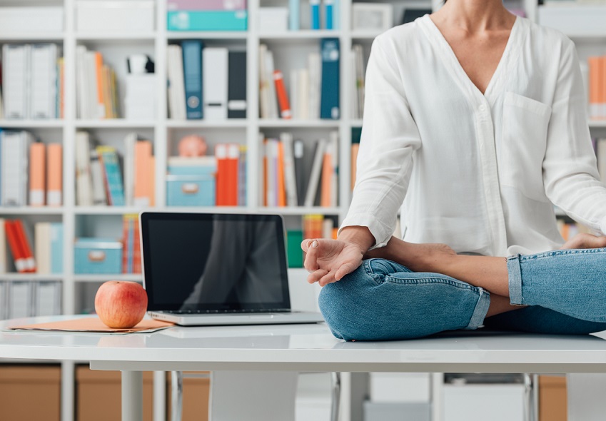 Relaxed woman practicing meditation at home, she is sitting in the lotus position on the office desk, mindfulness concept