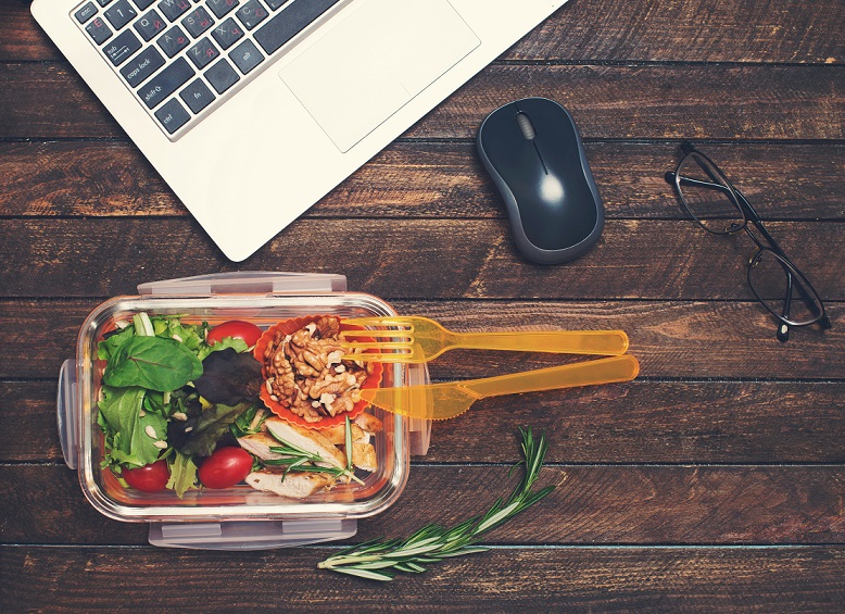 Healthy business lunch at workplace. Vegetables and fried chicken lunch box on working desk with laptop and glasses.